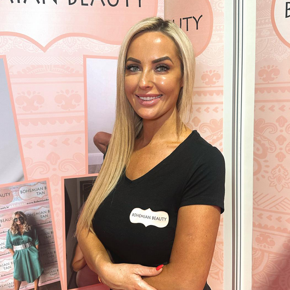 Woman in a black t-shirt standing in front of a pink 'Bohemian Beauty' booth.